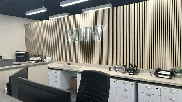 Halo-lit brushed stainless steel MHW letters mounted on a wood slat reception wall