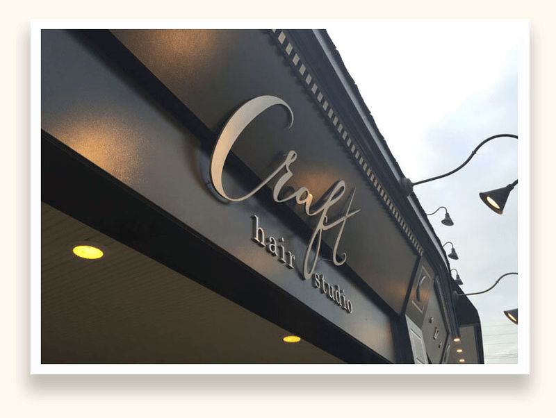 Brushed metal script letters spelling Craft Hair Studio on a dark storefront fascia