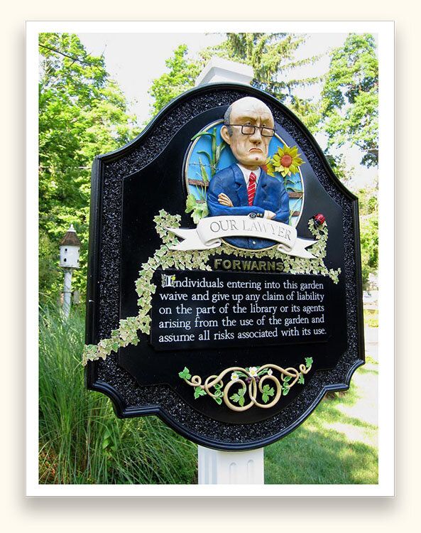 Black carved sign with a sculpted lawyer bust and ivy detail for a library garden liability notice