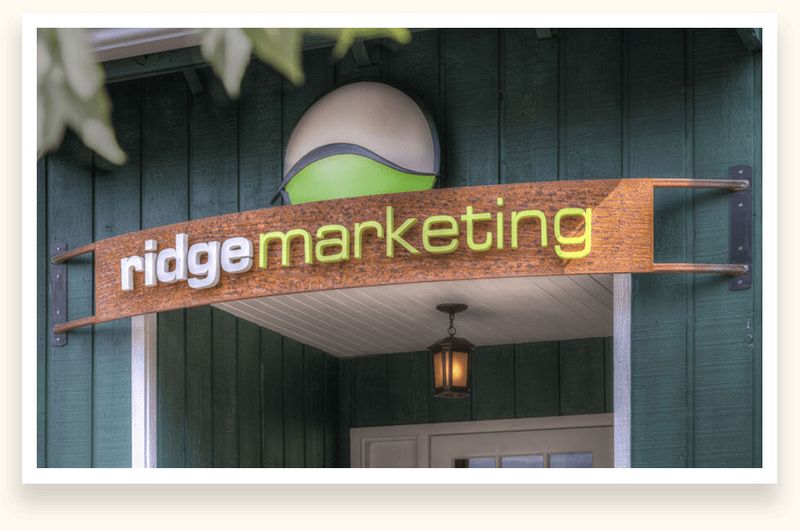 Curved wood-grain panel with dimensional white and green letters for Ridge Marketing