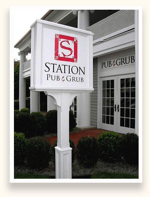 White post and panel sign with a red crest logo for Station Pub and Grub